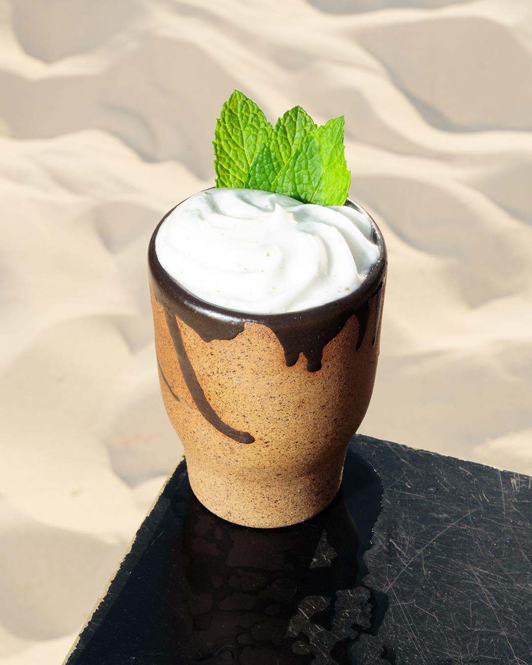 Drink servido em caneca de barro na areia