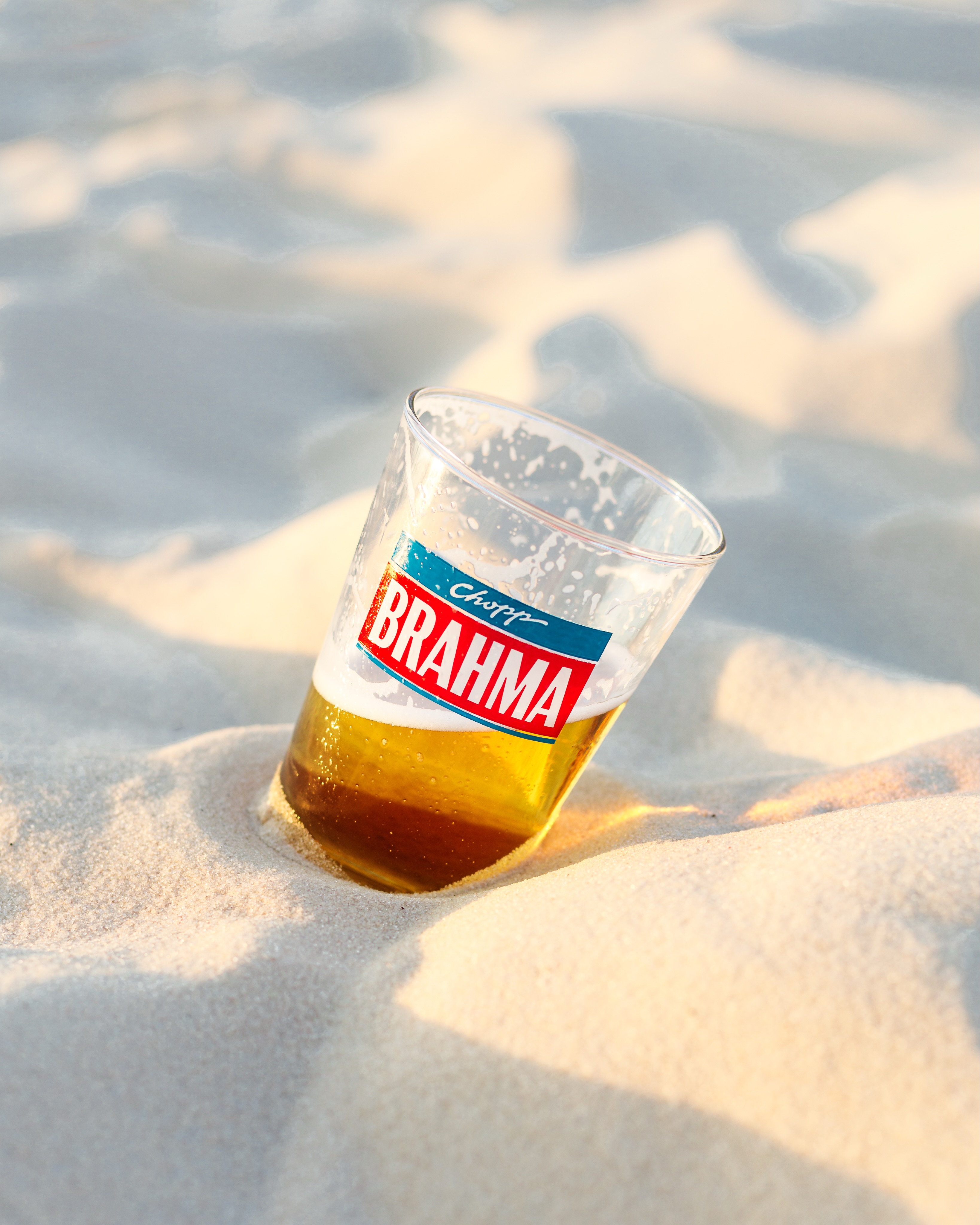 Chopp gelado enterrado na areia, luz dourada de fim de tarde